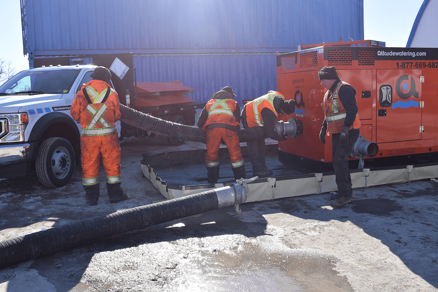 Two workers repairing a large orange pump, in an outdoor setting.