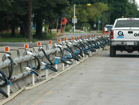 Ligne de tubes interconnectés le long d'une barrière en béton sur une route, avec un camion stationné à proximité.