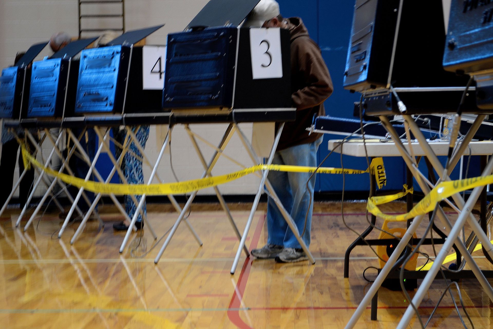 Voting booths in a gym, with one person standing at a booth numbered 3