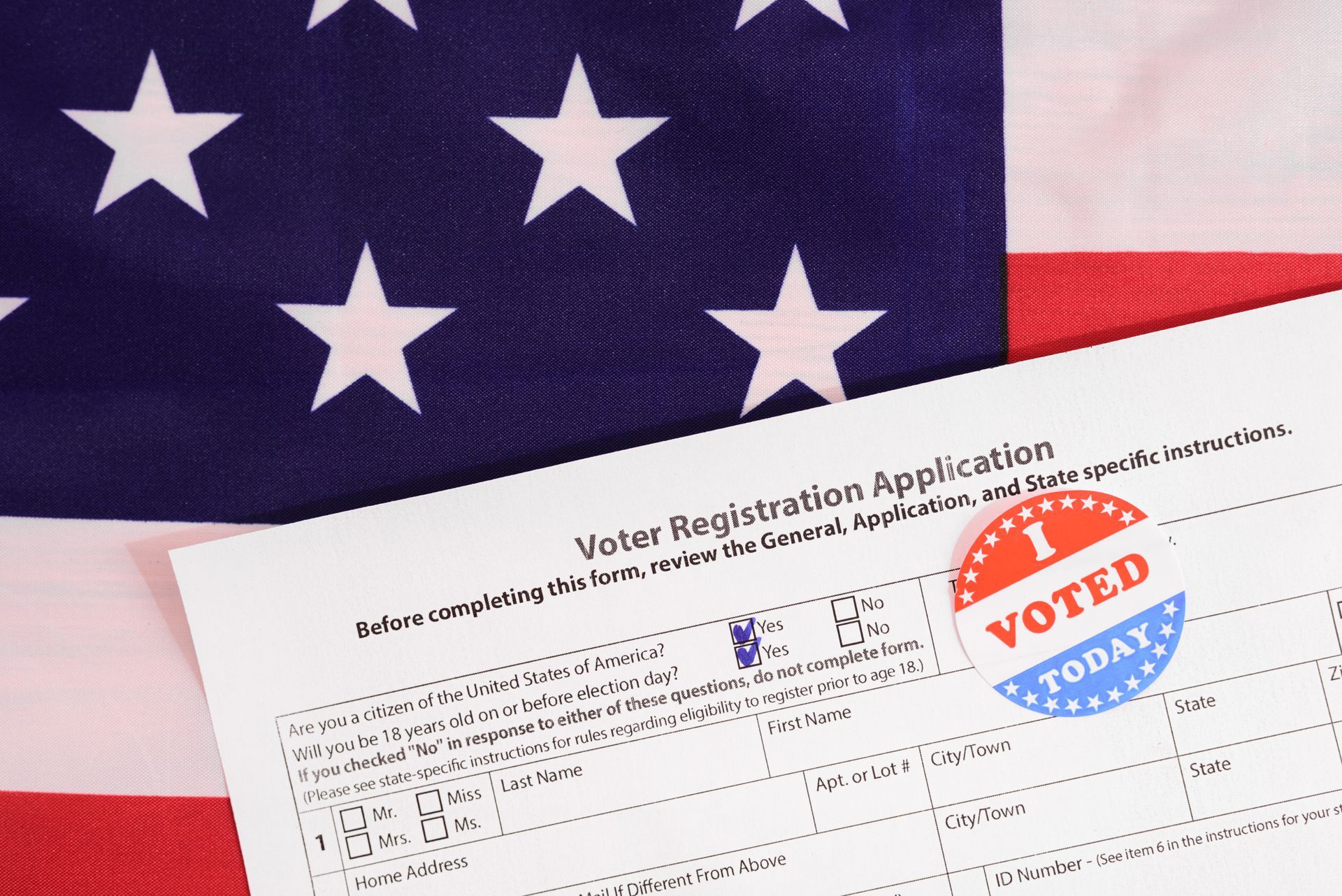 U.S. flag with voter registration form and red, white, and blue “Voted” sticker