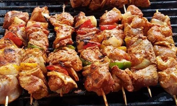 Gewürzte Fleisch- und Gemüsespieße werden auf einem Metallgrill zubereitet.
