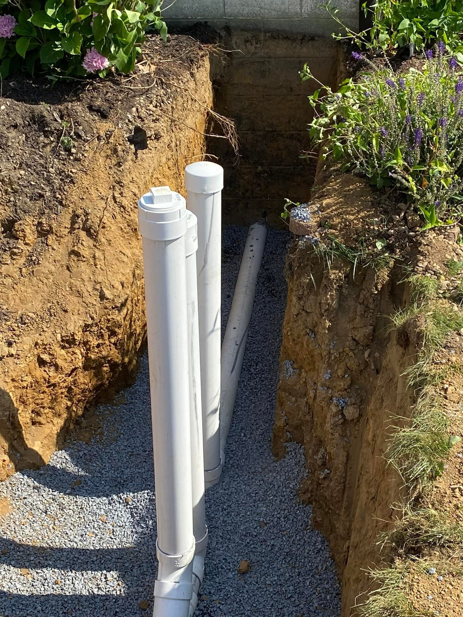 A row of white pipes are sitting in a trench in the dirt.