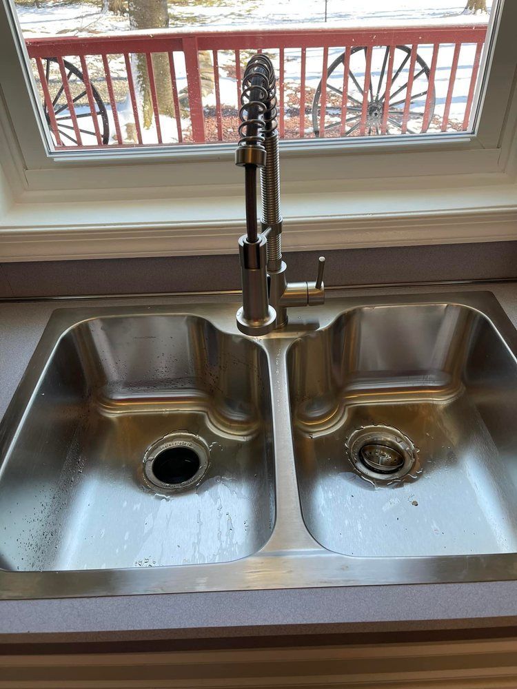A stainless steel kitchen sink with a faucet and a window in the background.