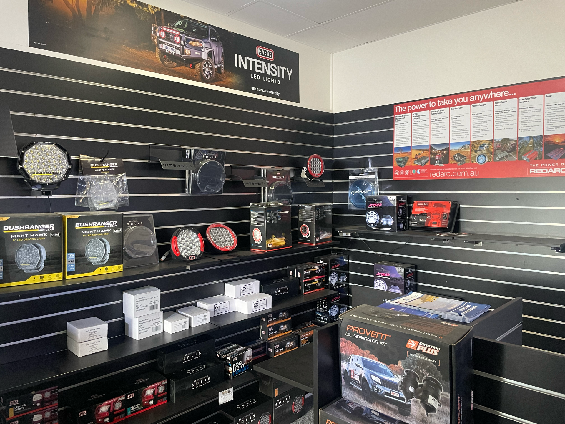 Auto parts display room with shelves of wheels, lights, and boxed accessories in a black-and-red showroom — Stay on Track 4X4 Accessories in Gladstone Central, QLD