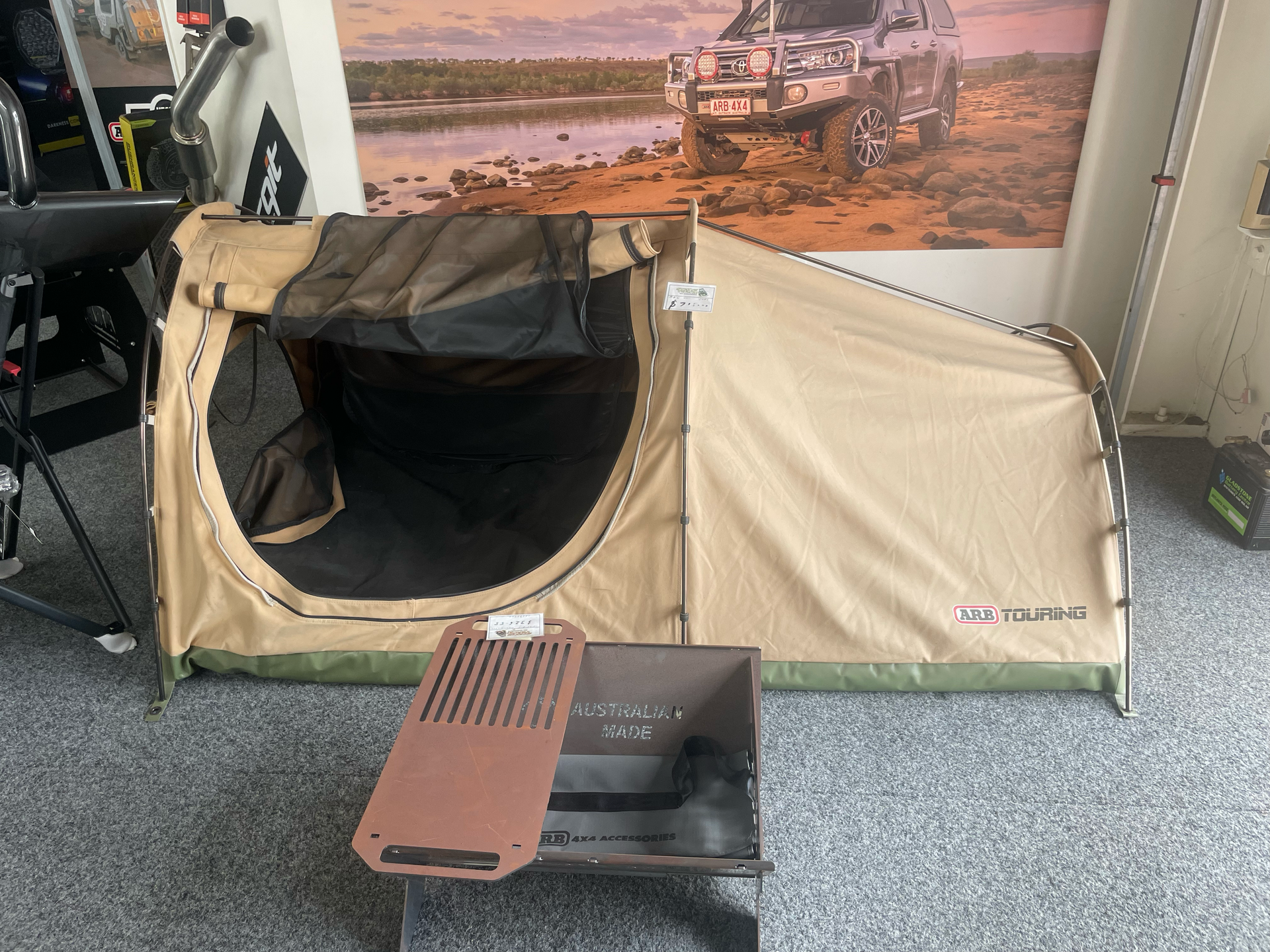 Beige camping tent with open front, pitched indoors on gray carpet beside a poster backdrop. — Stay on Track 4X4 Accessories in Gladstone Central, QLD
