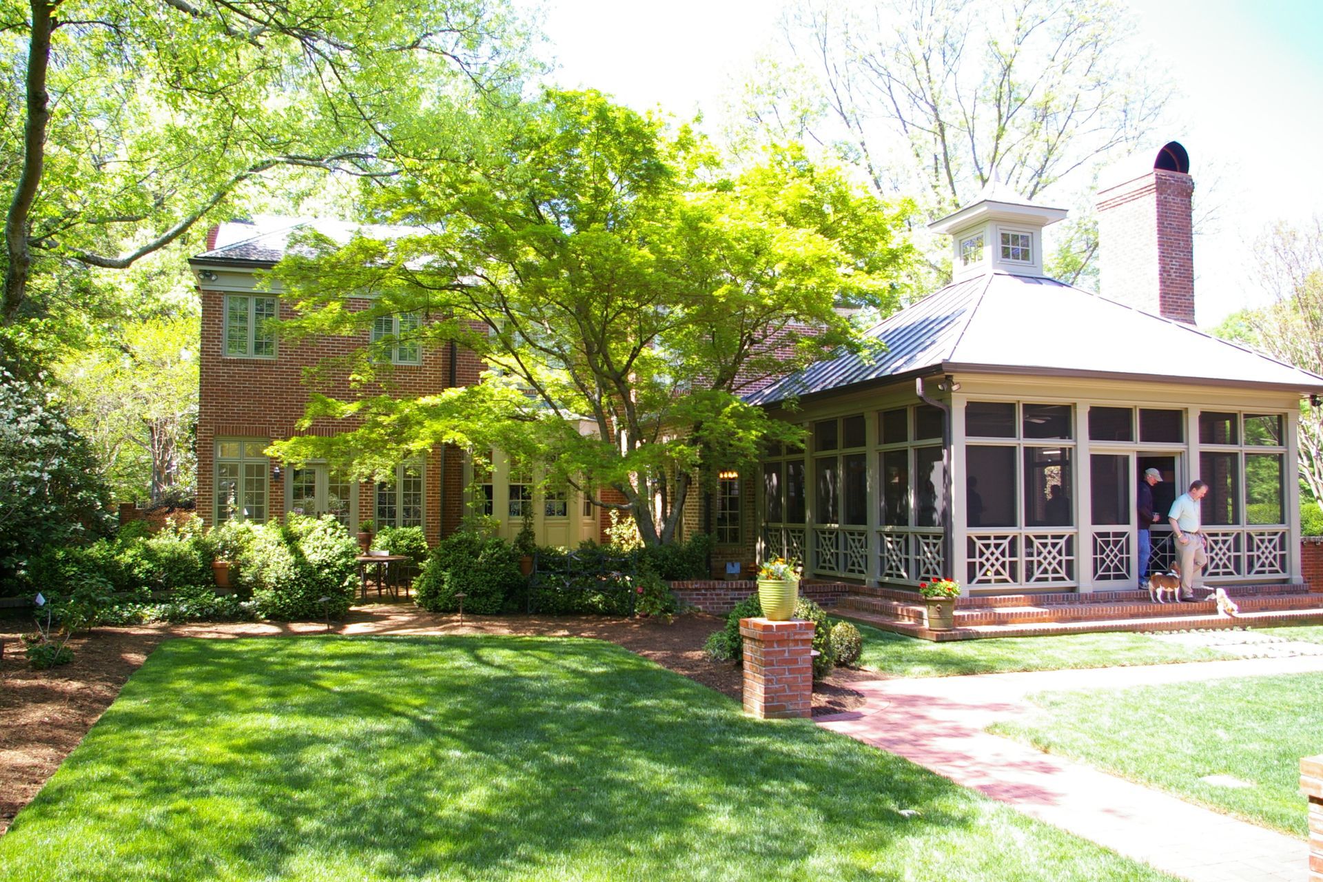 Brick house with a screened porch and brick chimney, surrounded by green trees and a manicured lawn.