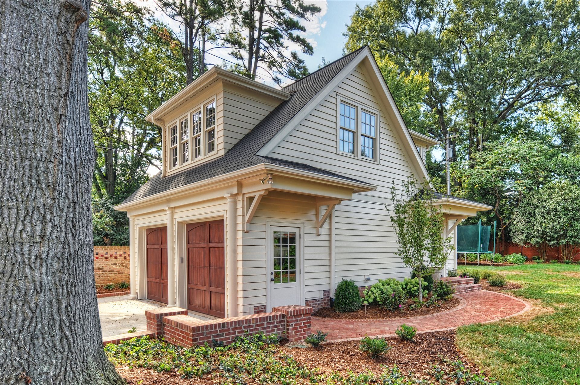 Small garage apartment with stained wood doors and gray roof in a wooded yard