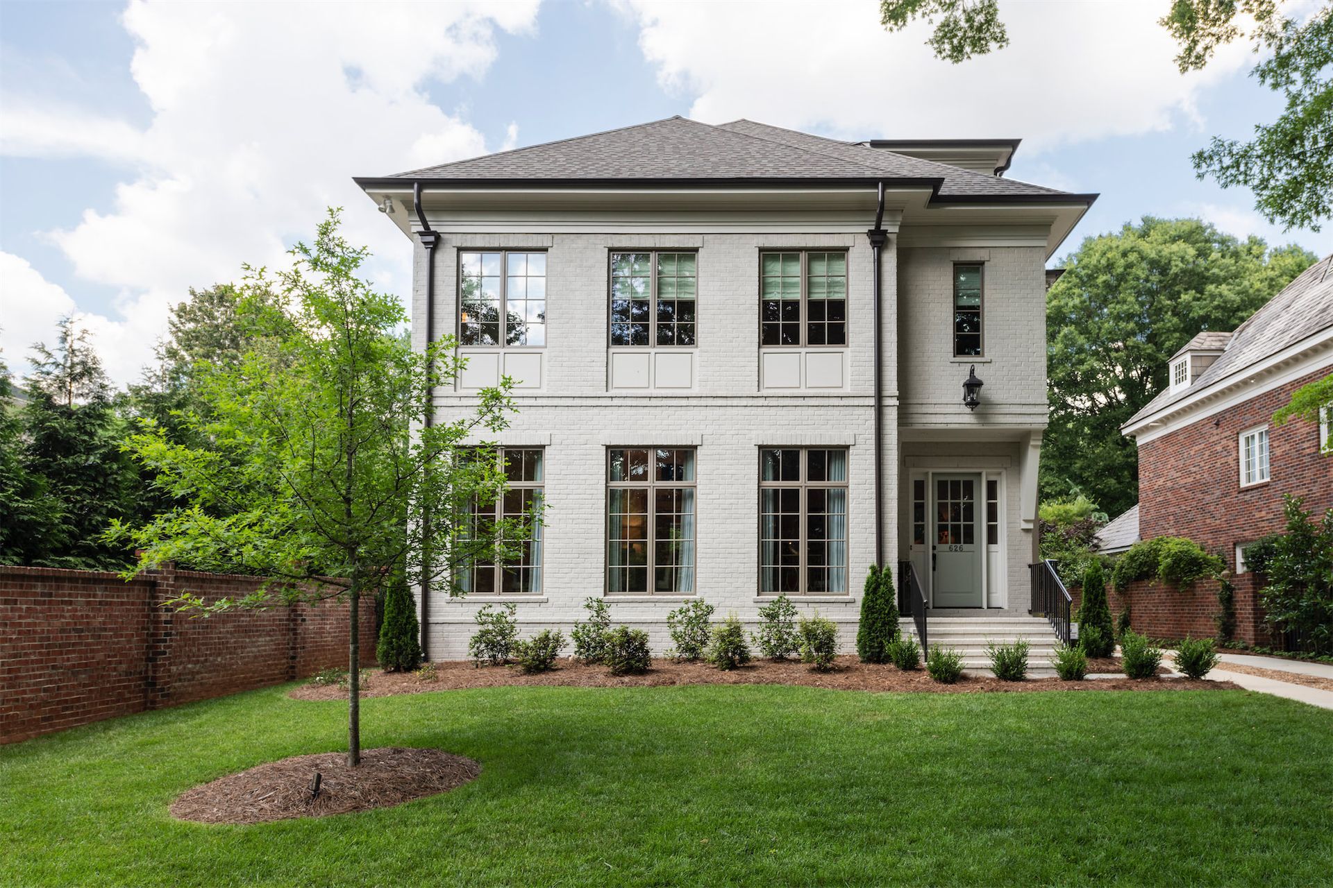 A large white house with a lot of windows is sitting on top of a lush green lawn.