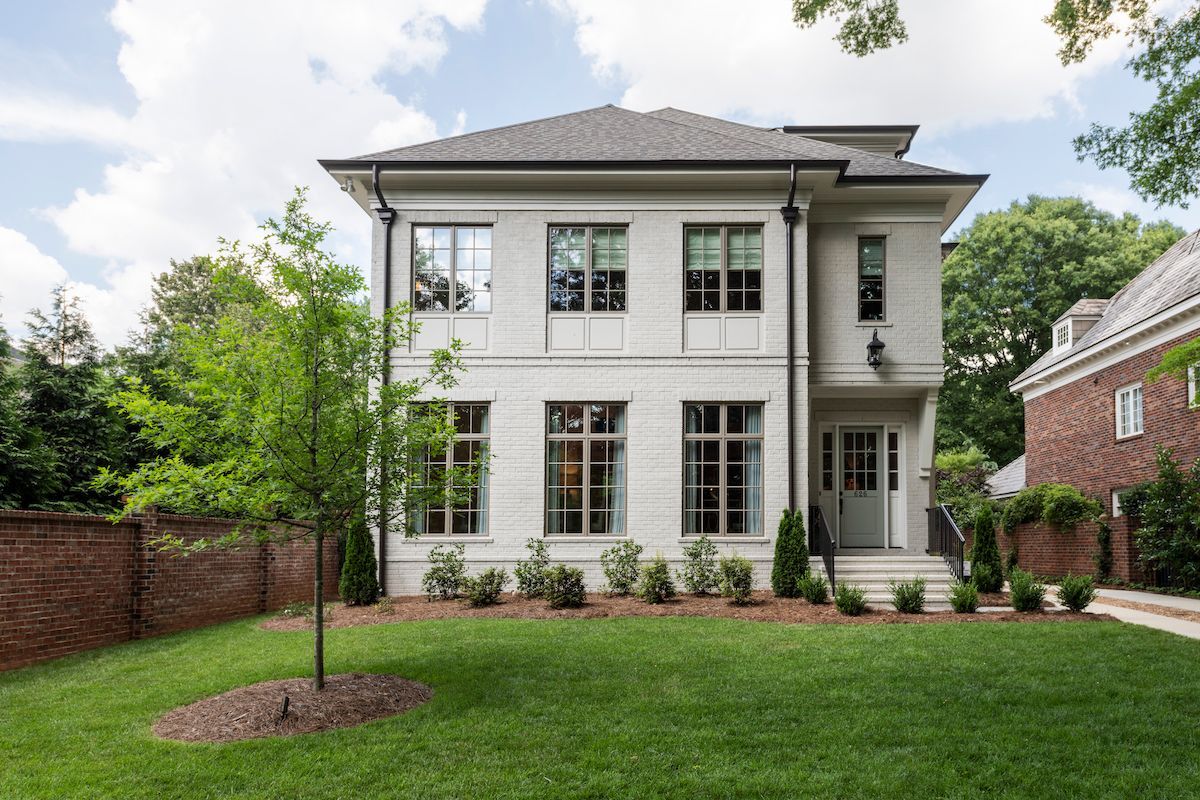 A large white house with a lot of windows is sitting on top of a lush green lawn.