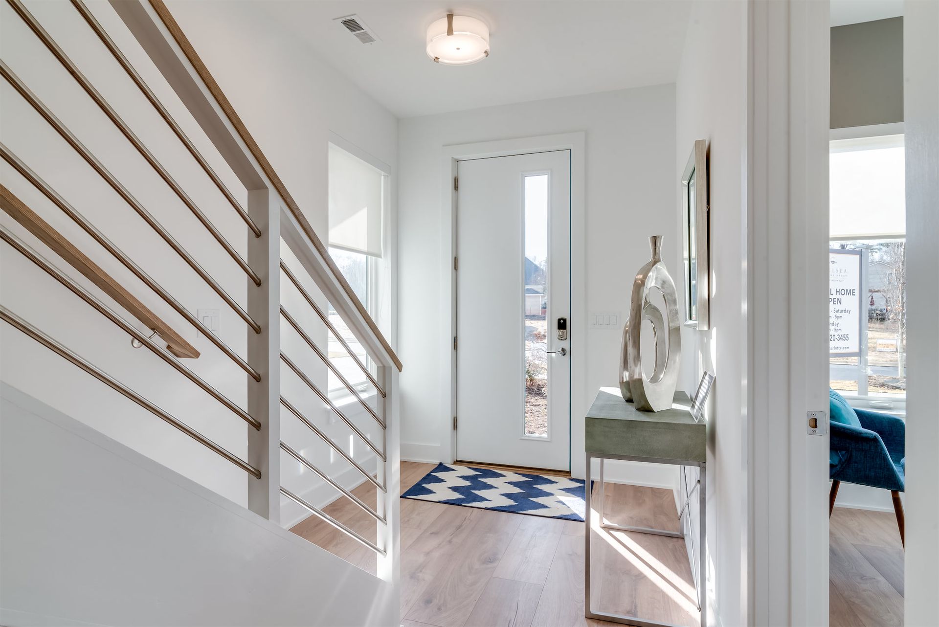 Bright hallway with staircase railing, narrow front door, console table, and blue-and-white tile floor.