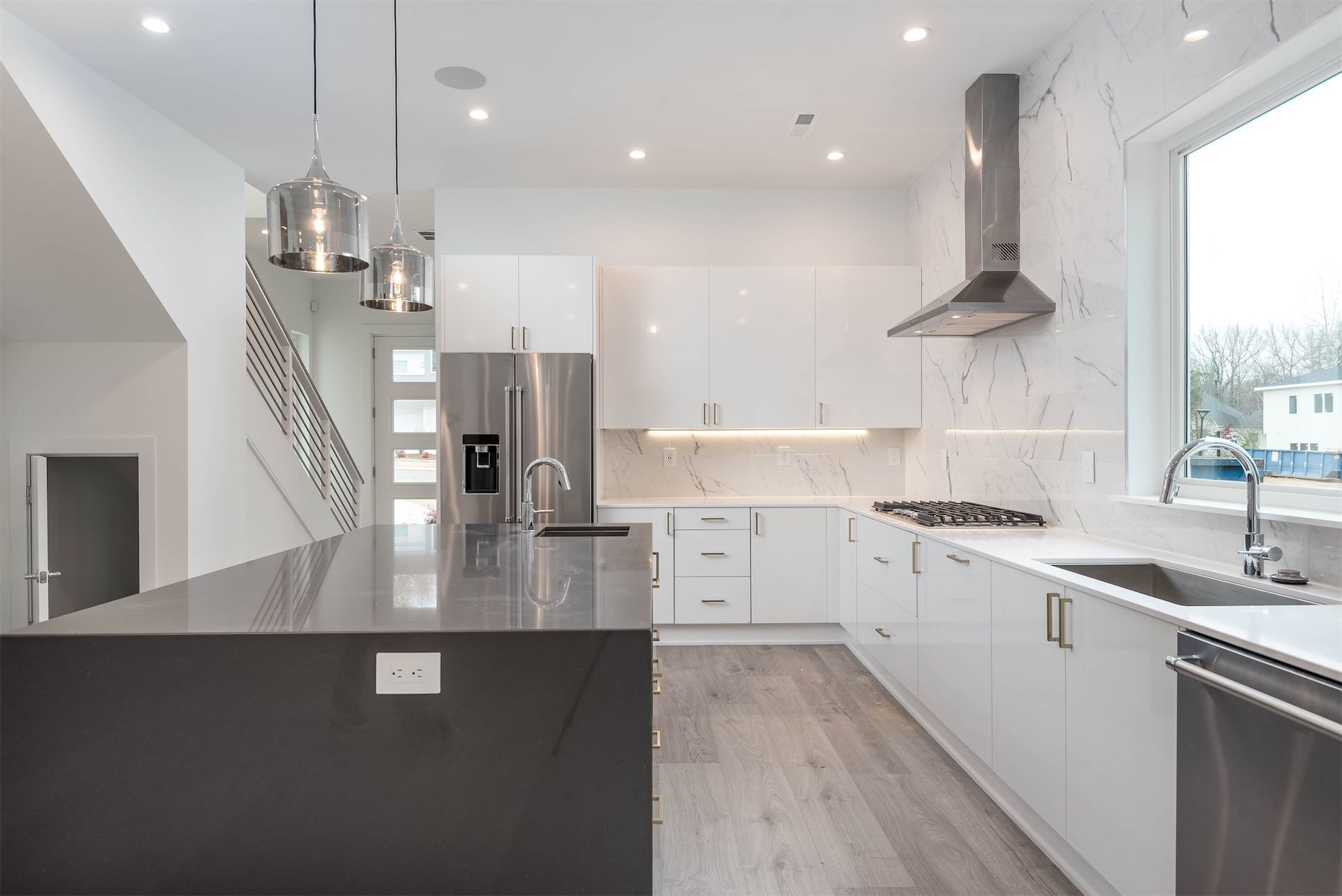 Modern white kitchen with black island, stainless appliances, and large window