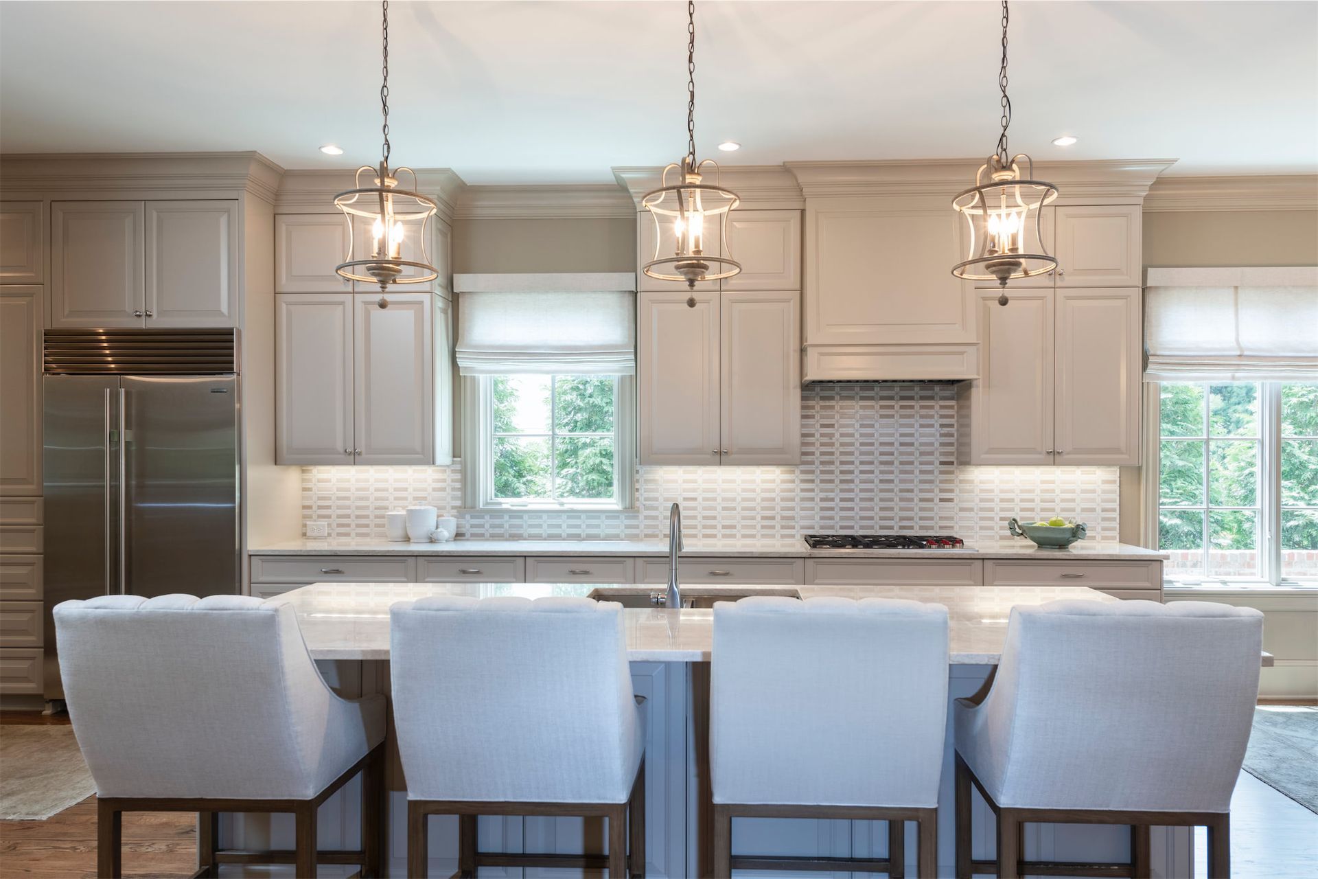 A kitchen with white cabinets and stools and a large island.