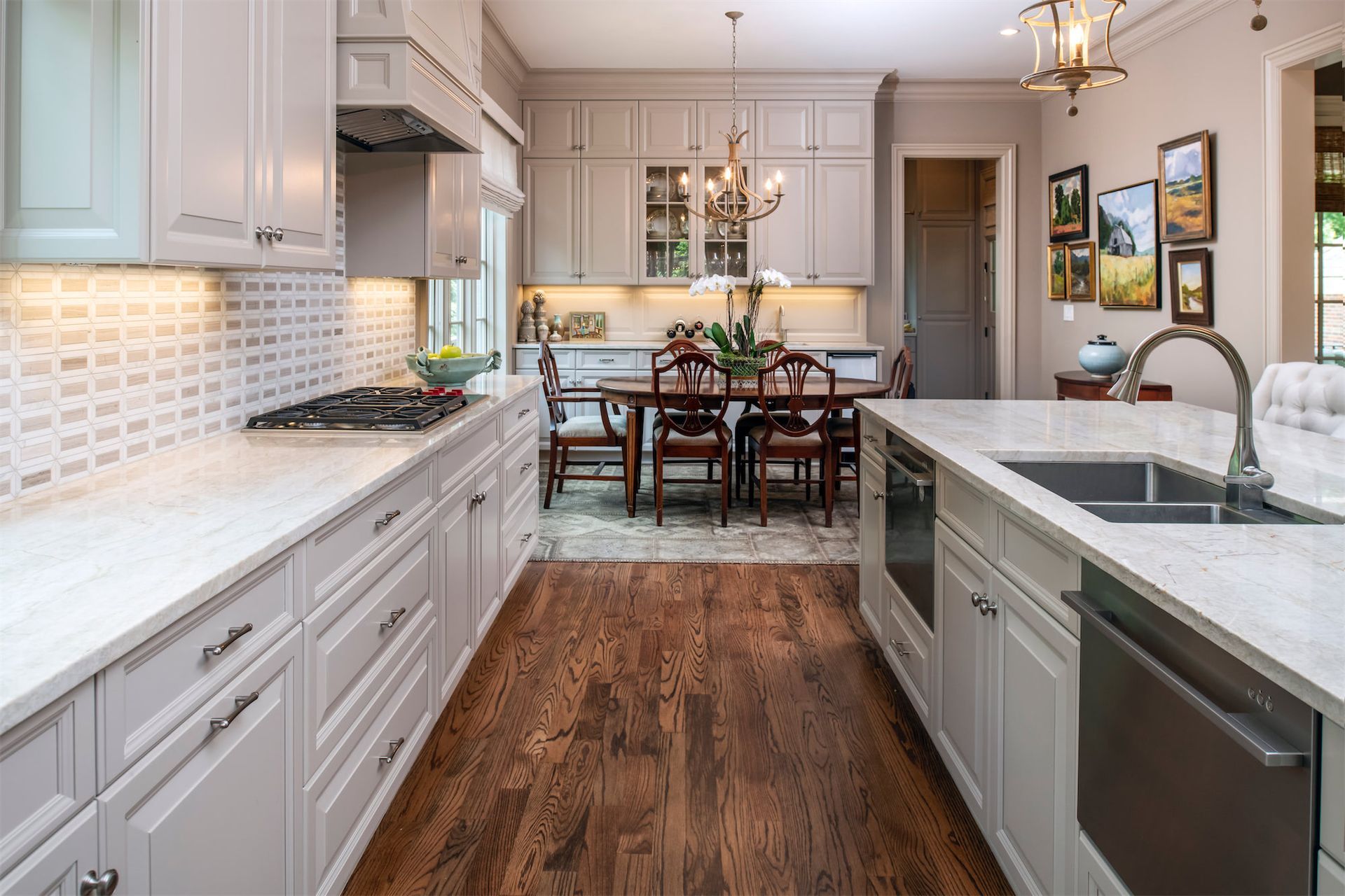 A kitchen with white cabinets and hardwood floors and a dining room in the background.