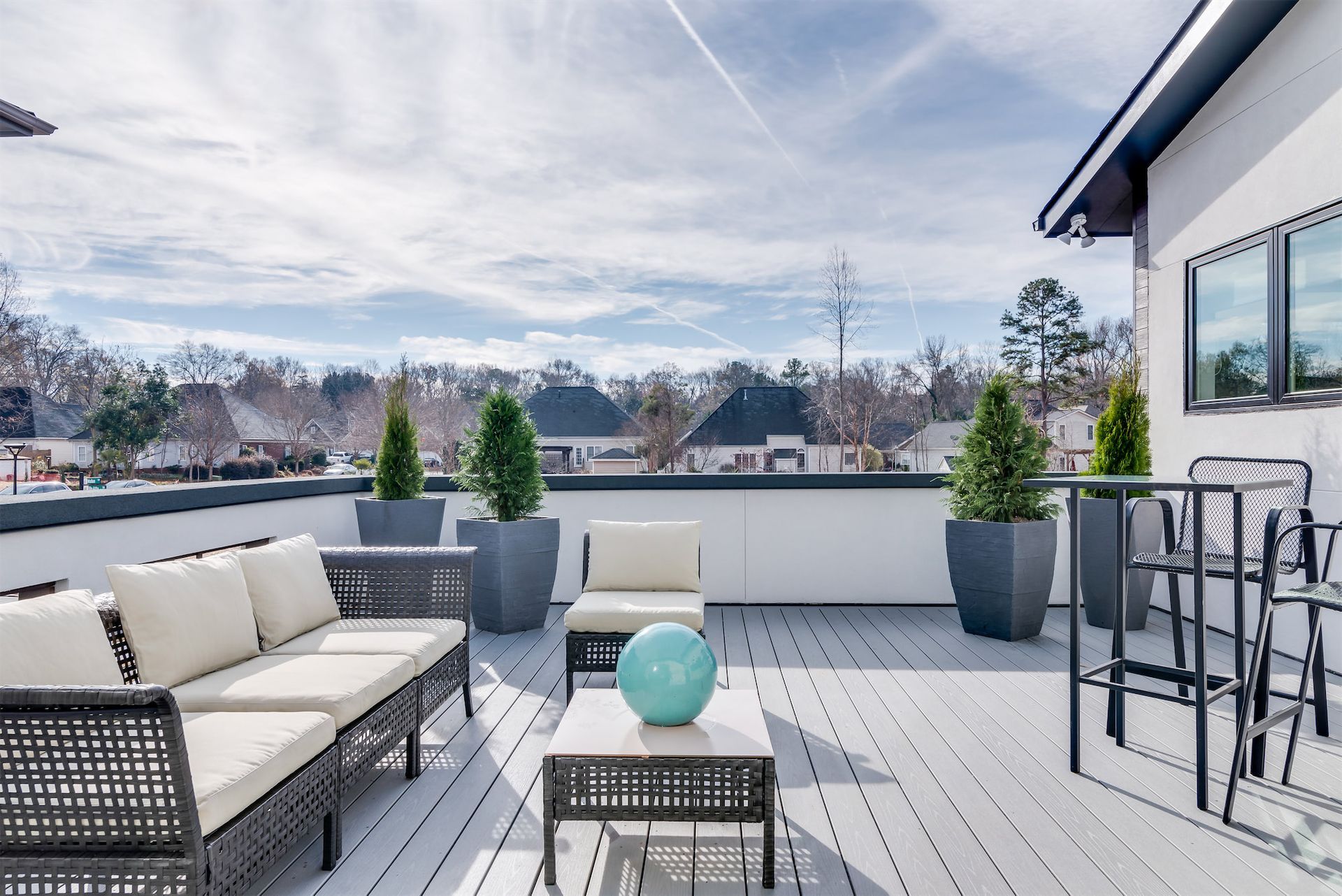 A rooftop deck with a couch , chairs , table and potted plants.