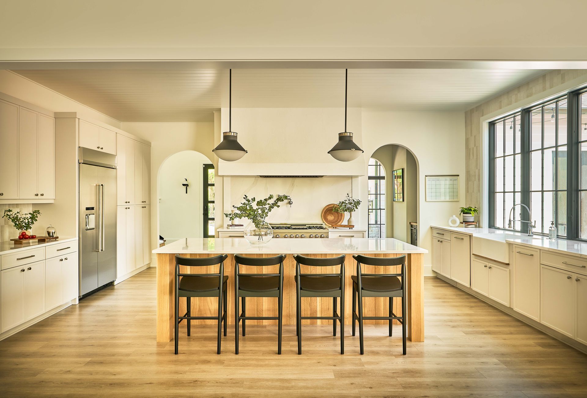 Bright modern kitchen with island, stools, pendant lights, and large windows