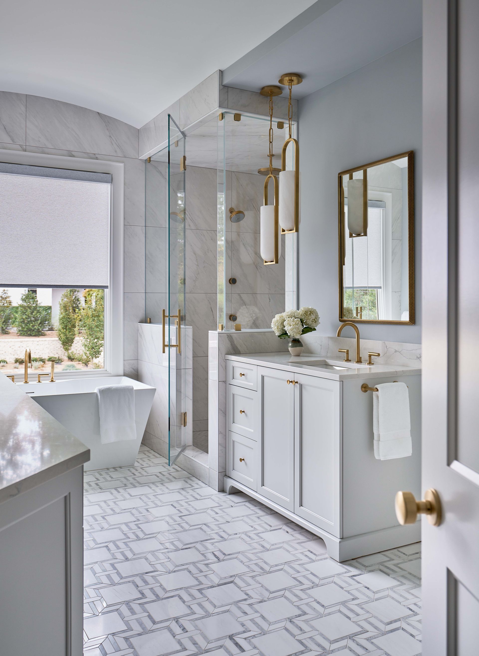 Eastover, Charlotte. Bright bathroom with glass shower, double vanity, gold fixtures, and hex tile floor.