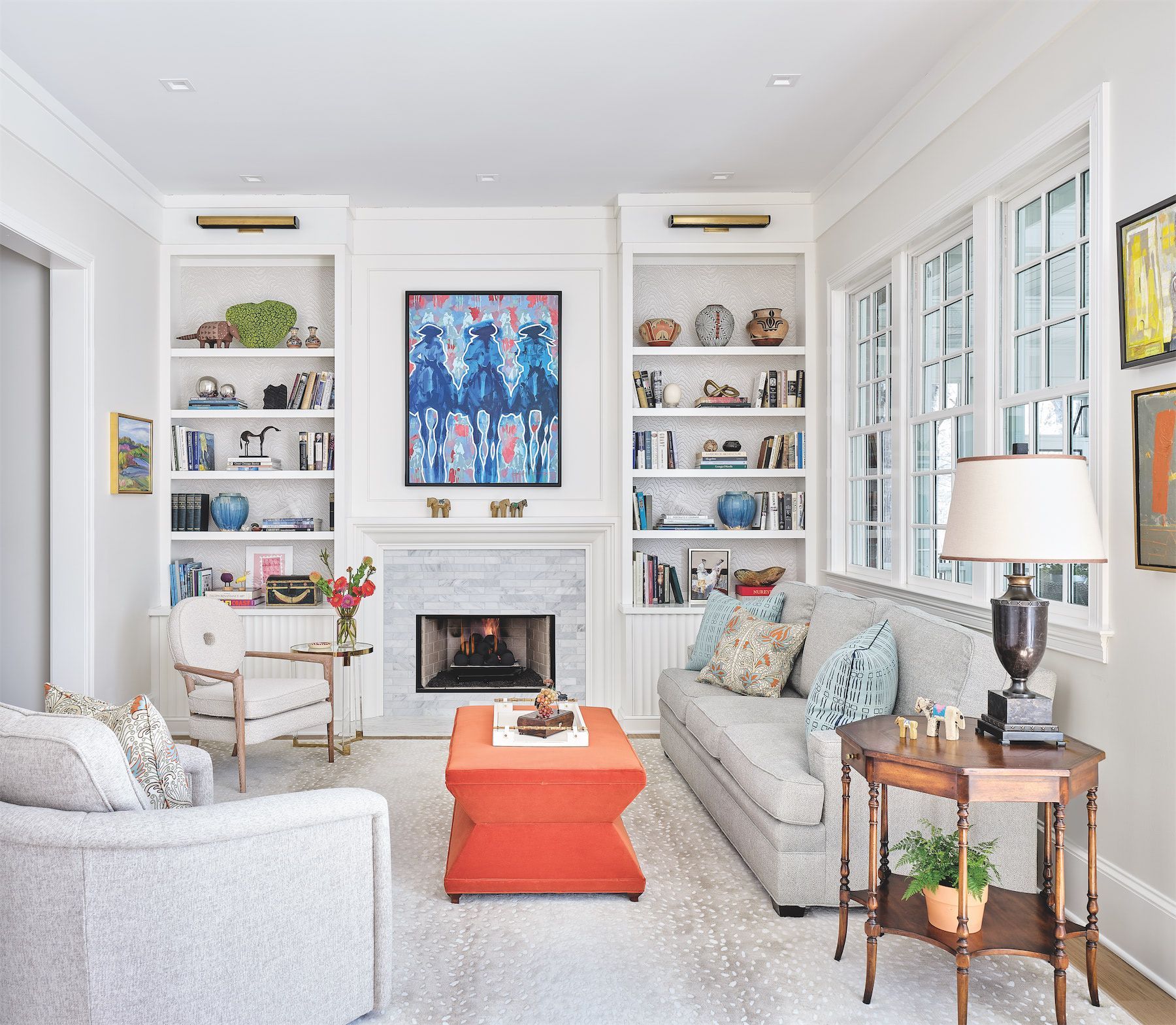 Bright living room with white built-ins, fireplace, orange ottoman, and floral sofas