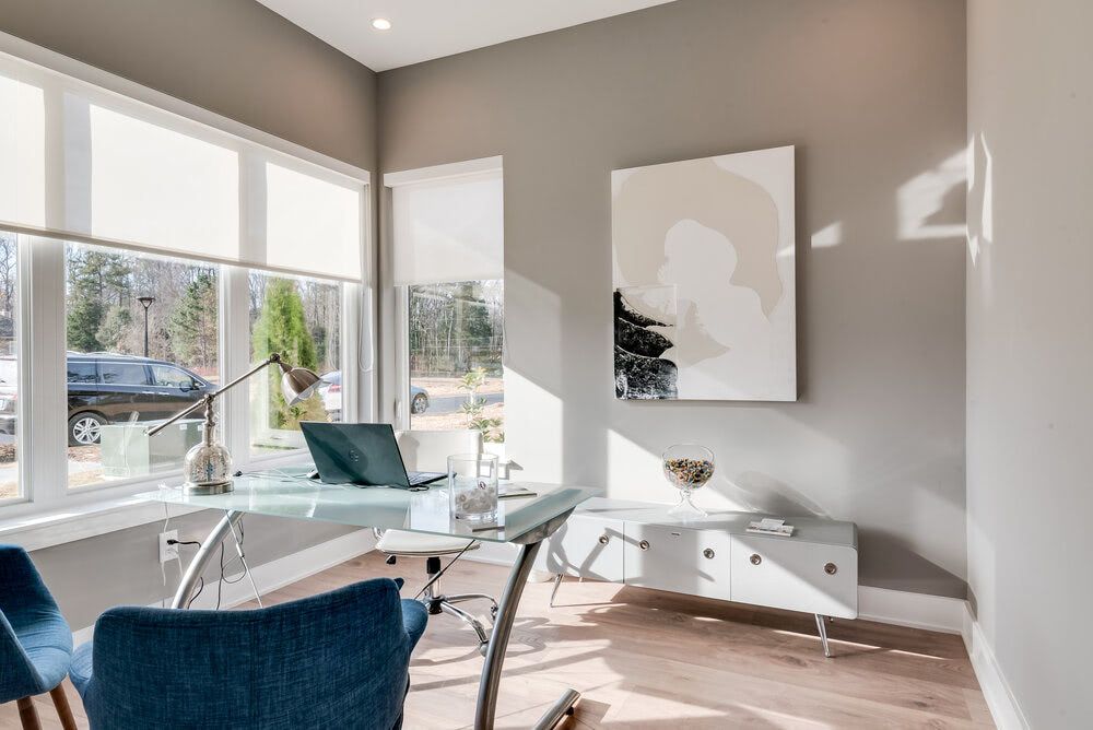 A home office with a desk and chairs and a large window.