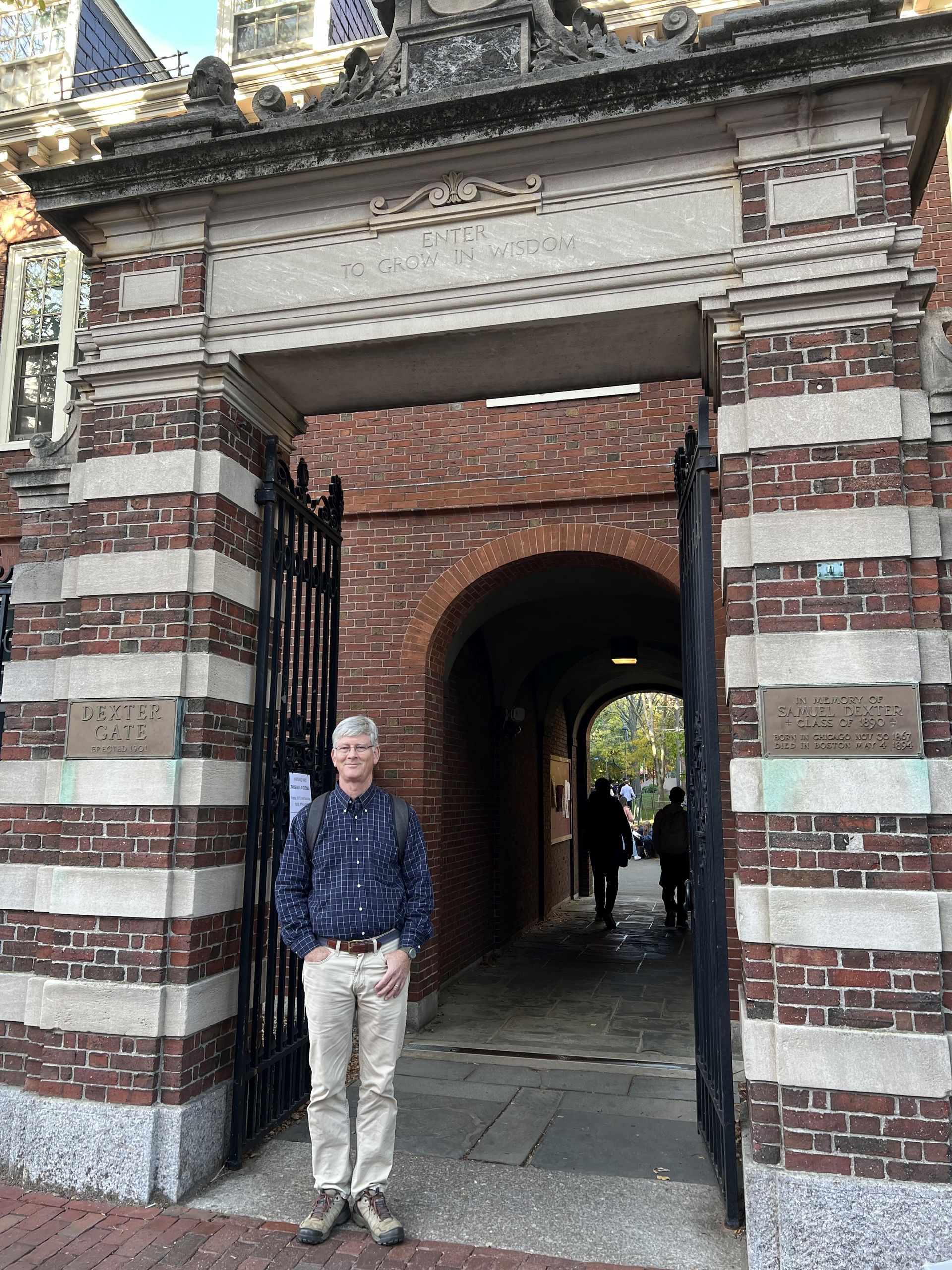 Person standing in a brick archway of Harvard Yard with red-and-white striped masonry and a tunnel behind him