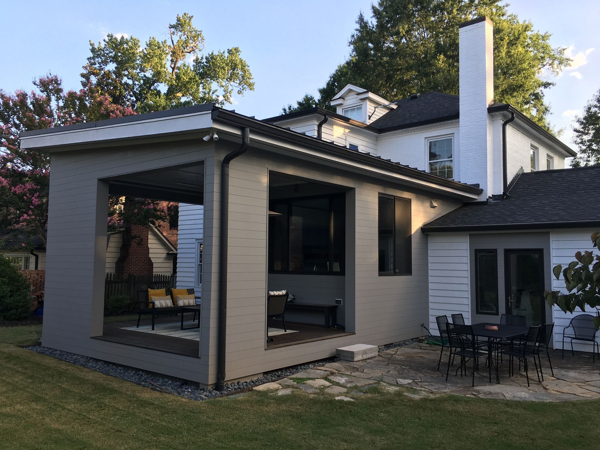 The back of a house with a porch and a table and chairs in the backyard.