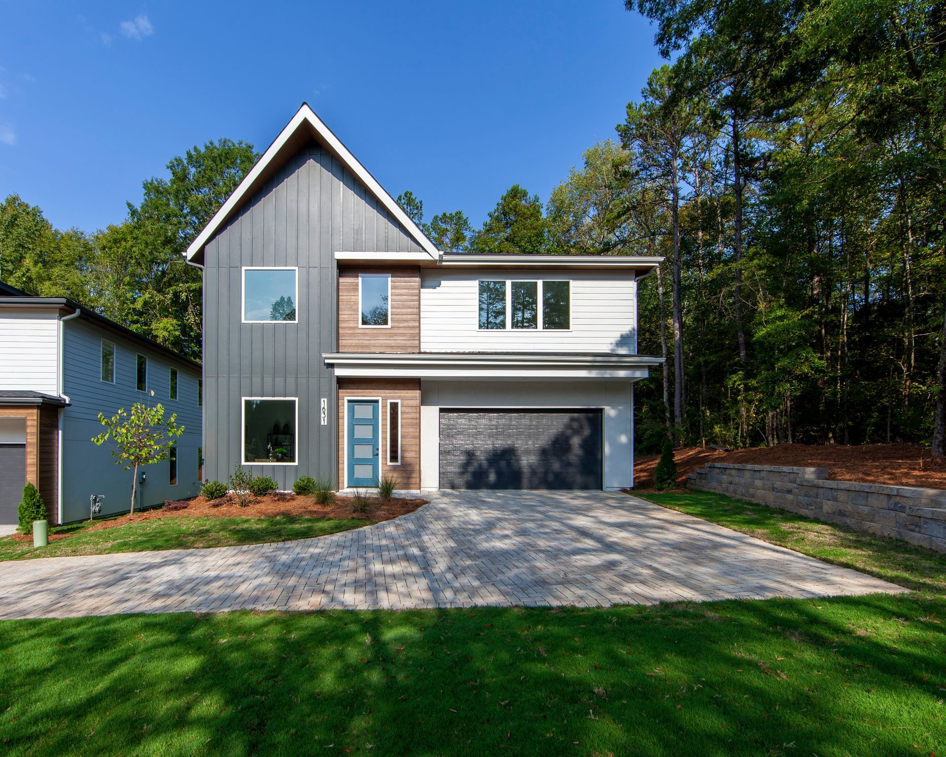 A modern house with a garage and a driveway is surrounded by trees.