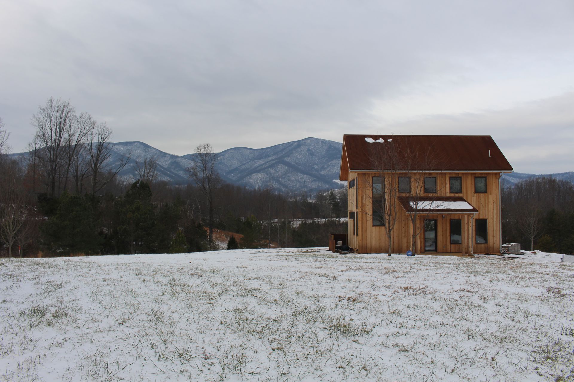 Snowy field with a small wooden house and mountains under a cloudy sky