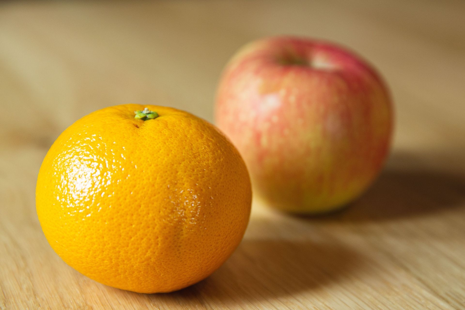 Orange and apple on a wooden table, with the orange in sharp focus