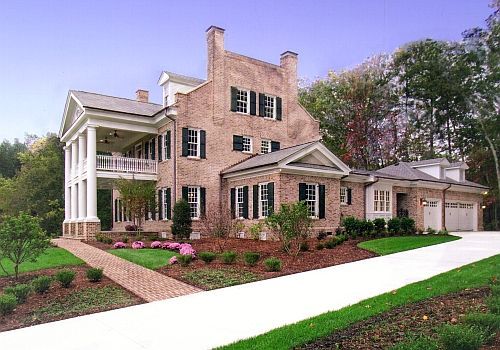Large brick suburban house with white columns, front porch, attached garage, and landscaped yard