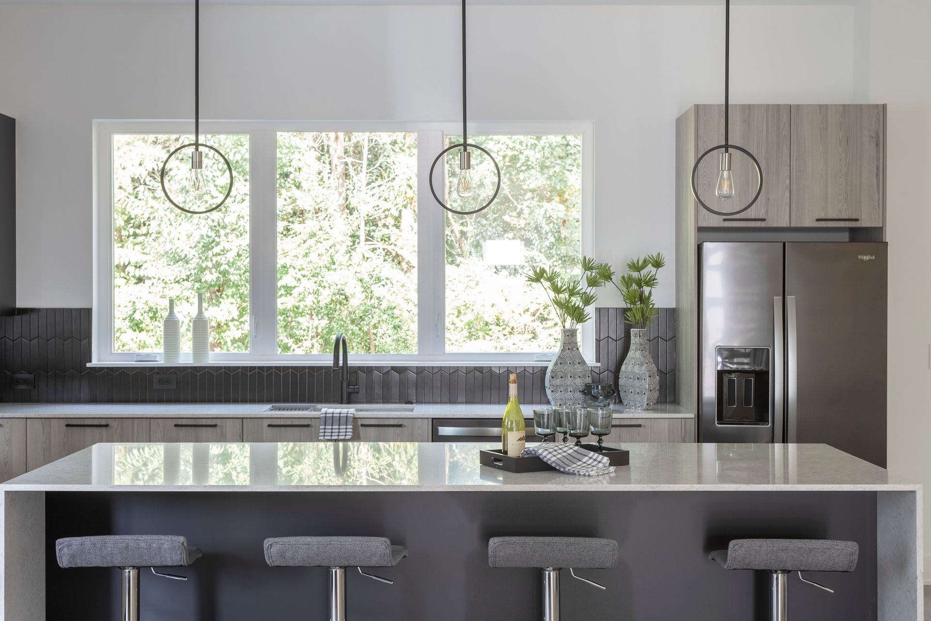 A kitchen with a large island , stools , a refrigerator and a window.