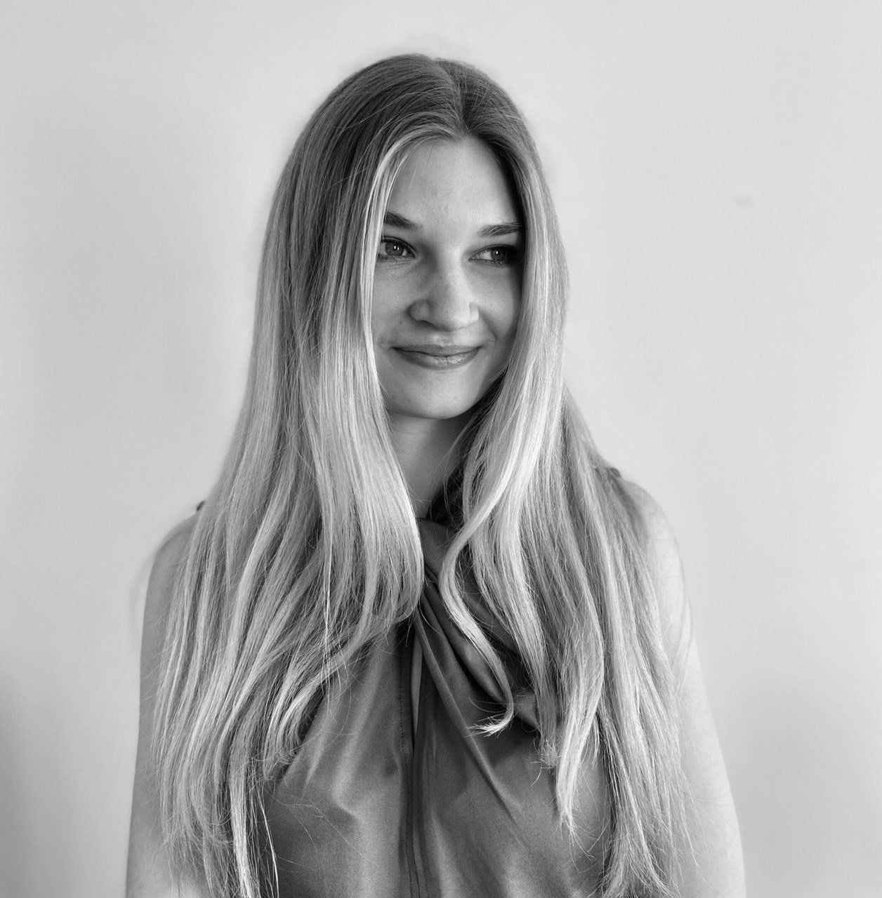 Eine Frau mit langen blonden Haaren lächelt auf einem Schwarzweißfoto.