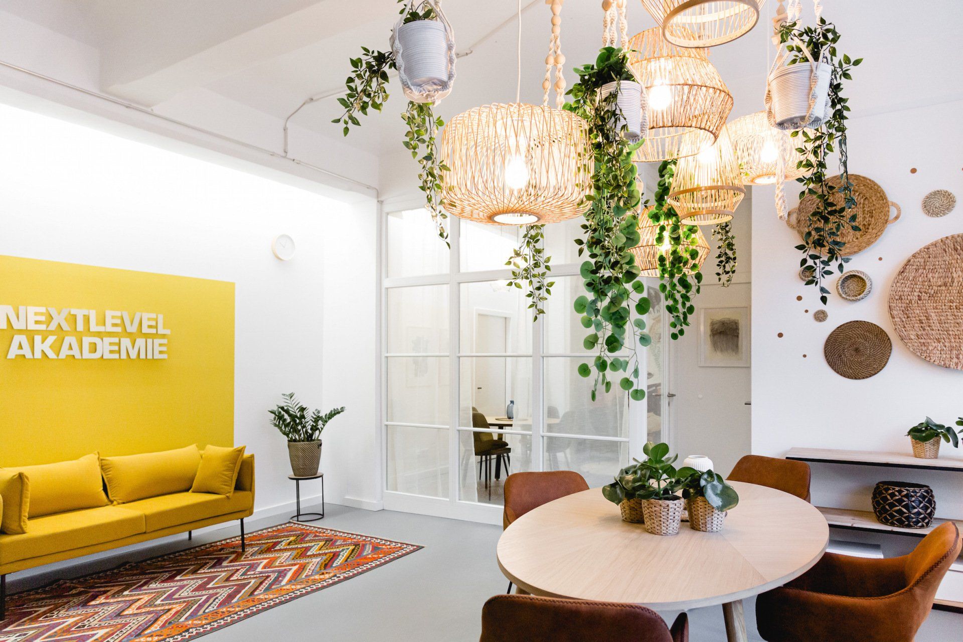 Ein Wohnzimmer mit einer gelben Couch und einem Tisch, von dessen Decke Pflanzen hängen.