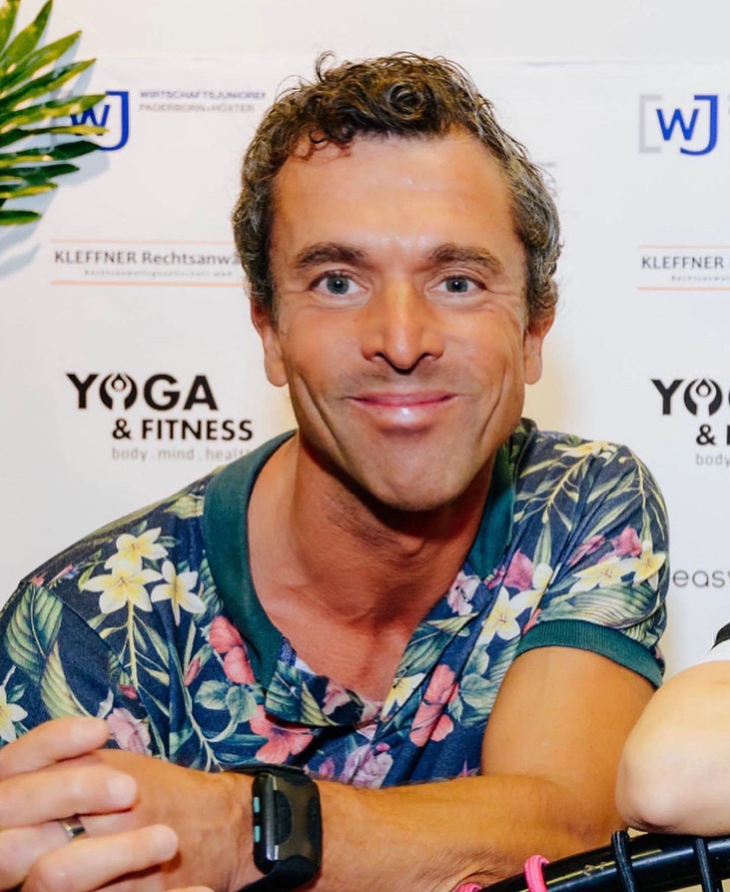 Ein Mann lächelt vor einem Yoga- und Fitnessschild