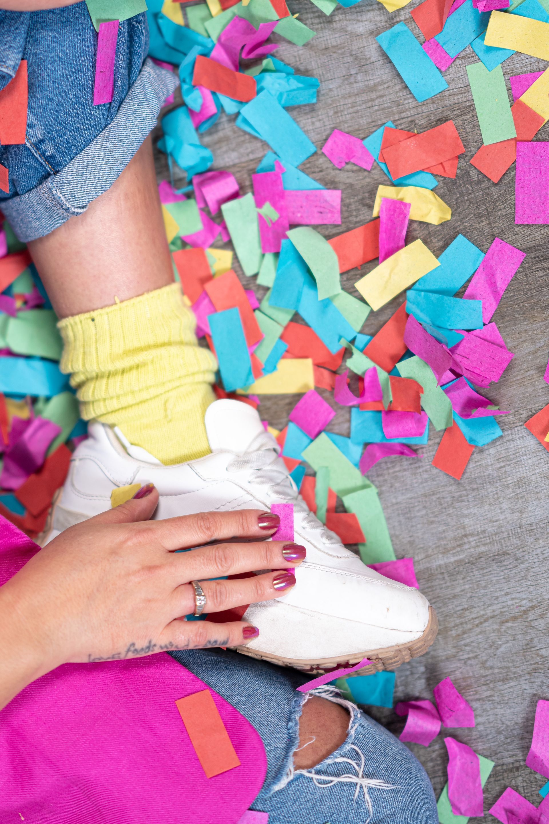 Hände halten einen weißen Turnschuh inmitten bunter Konfetti auf grauem Boden