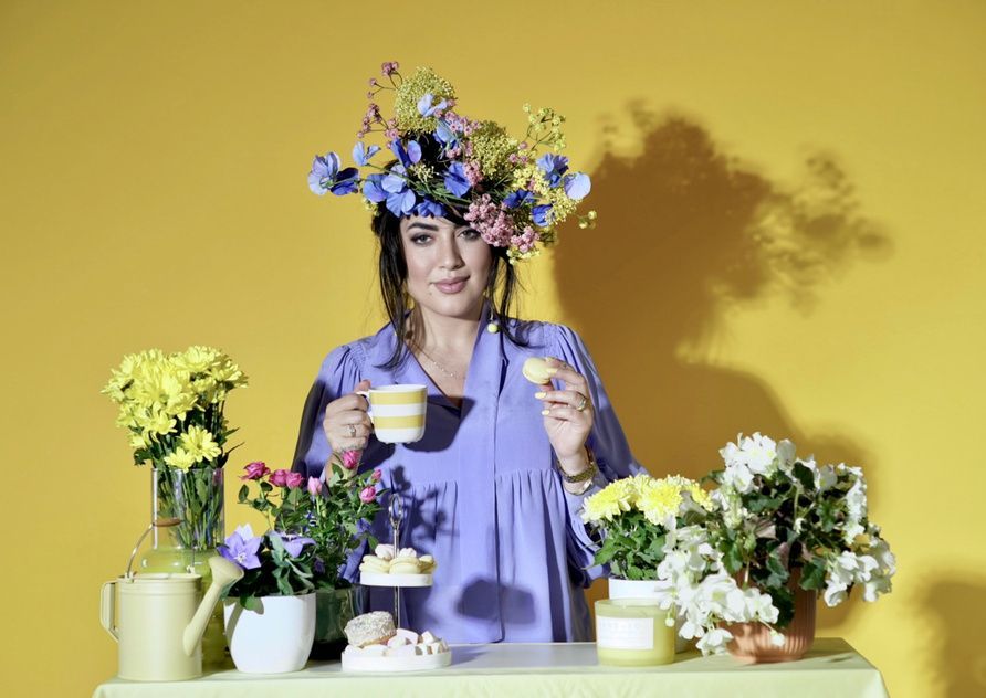 Eine Frau mit einem Blumenkranz auf dem Kopf sitzt an einem Tisch mit Blumen.