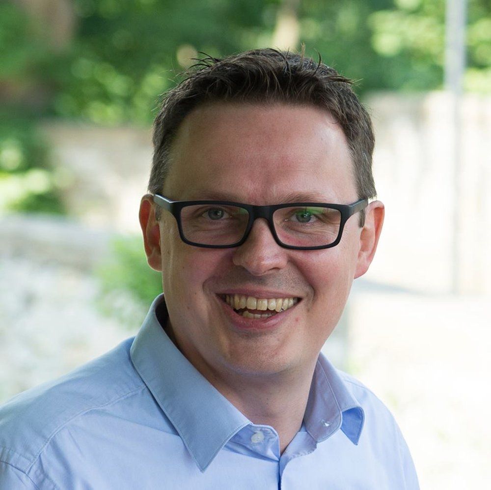 Ein Mann mit Brille und blauem Hemd lächelt in die Kamera