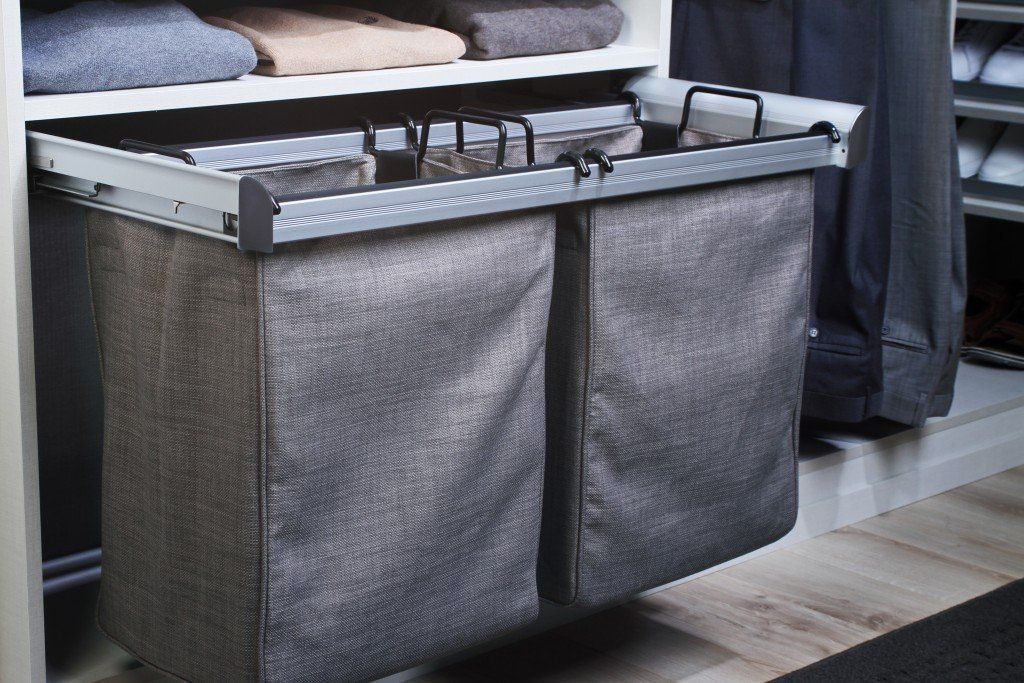 A laundry basket is pulled out of a closet filled with clothes.