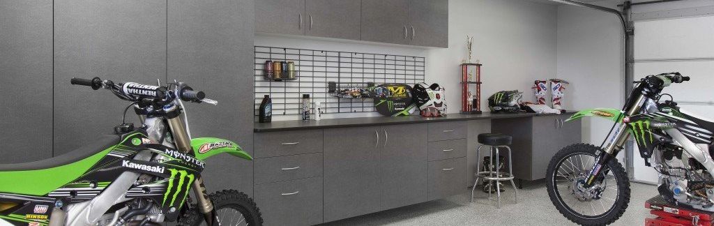 Two dirt bikes are parked in a garage next to each other.
