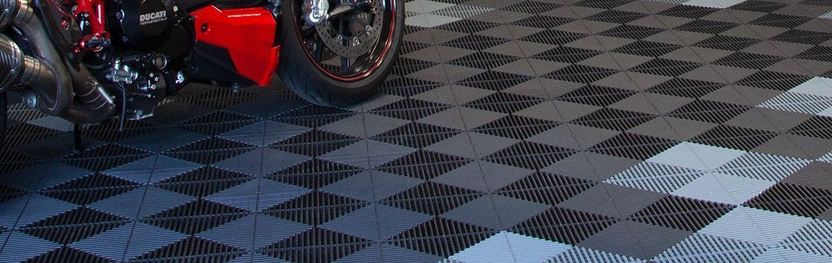 A motorcycle is parked on a swisstrax floor in a garage.