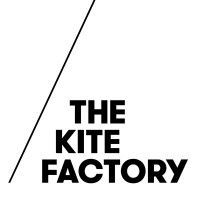 Het logo van The Kite Factory met zwarte tekst en een diagonale lijn op een witte achtergrond.