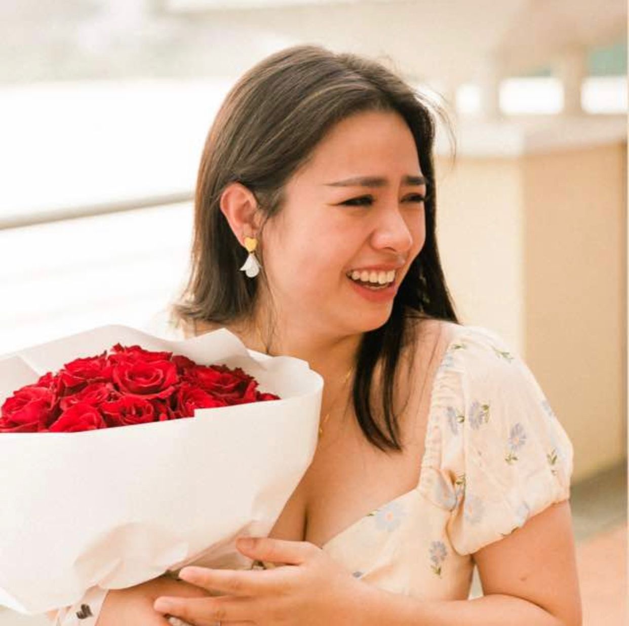 A woman is holding a bouquet of red roses and smiling.