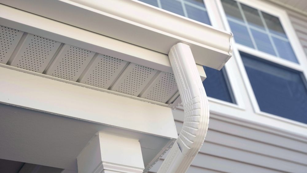 White house eaves with gutter and downspout beneath a window, shot from below