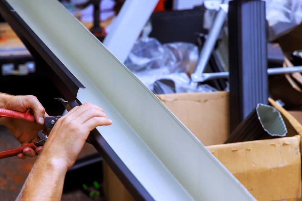 Hands installing a metal gutter section in a cluttered workshop area