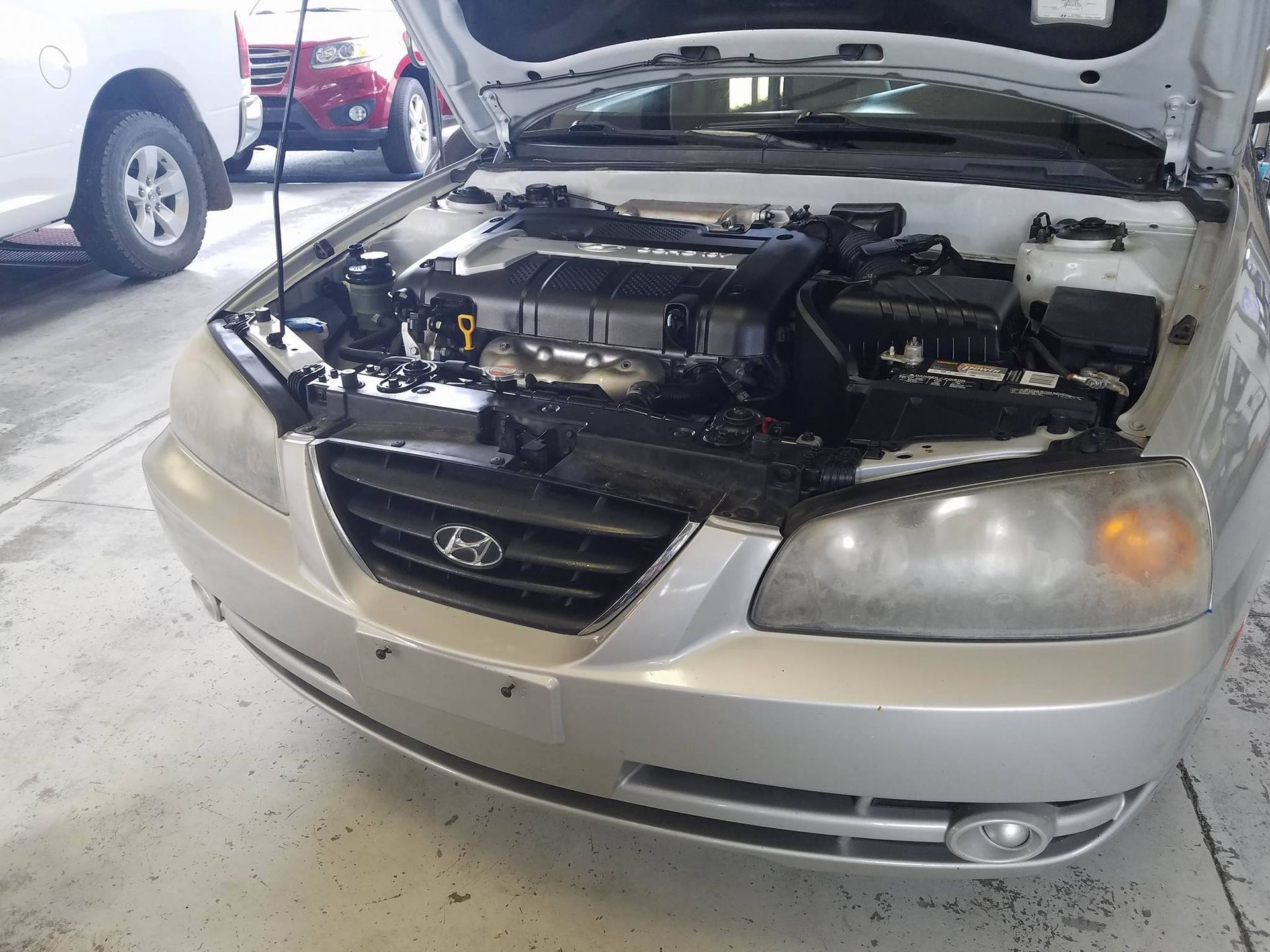 Silver Hyundai Elantra with open hood, showing the engine in a garage setting.