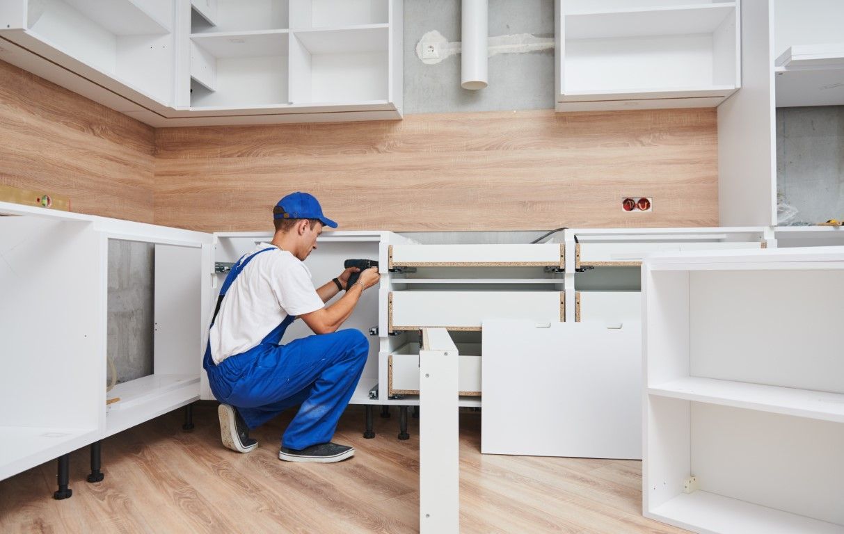 Worker in blue uniform inspecting cabinets in a bright unfinished kitchen cabinetry setup