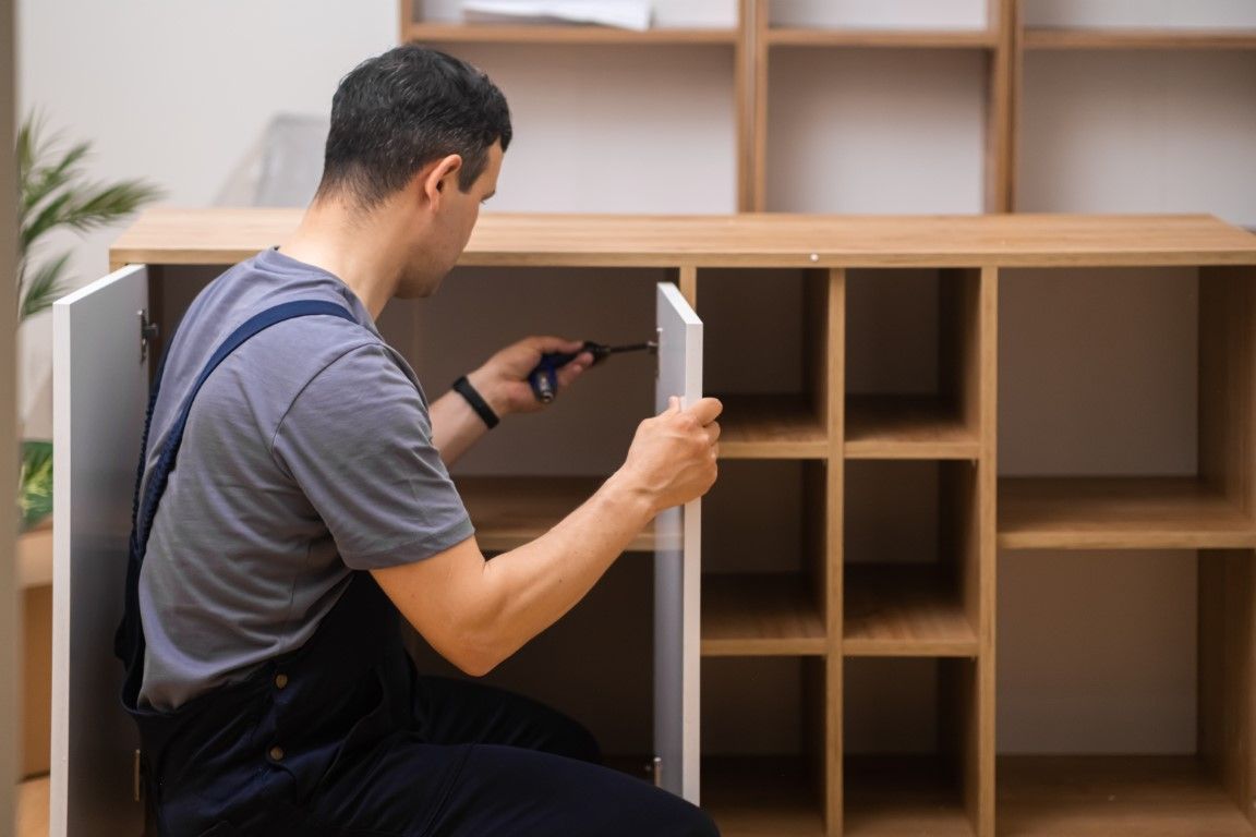 Person assembling a wooden cabinet with a screwdriver in a living room area