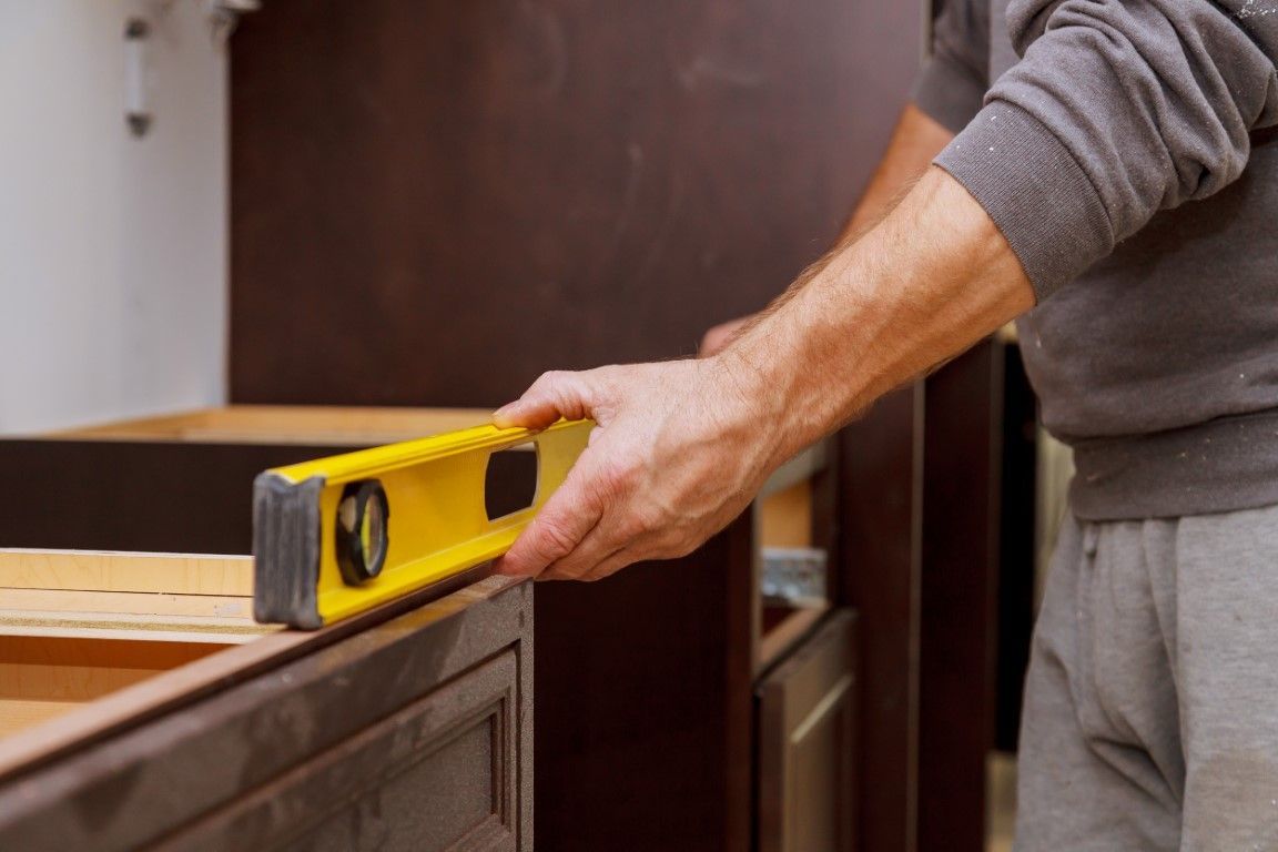 Person using a yellow level to measure a wooden cabinet surface