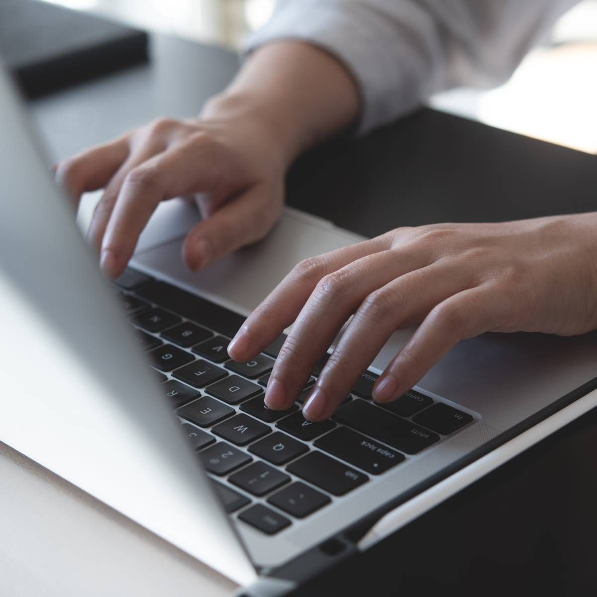 Hands typing on a silver laptop keyboard on a desk.