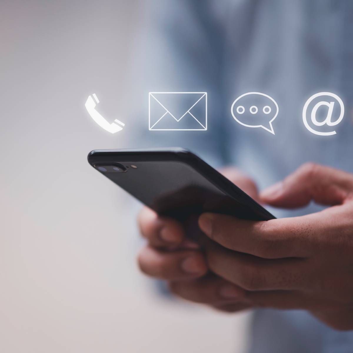 Person holding a smartphone with contact icons, including phone, email, chat, and at symbol.