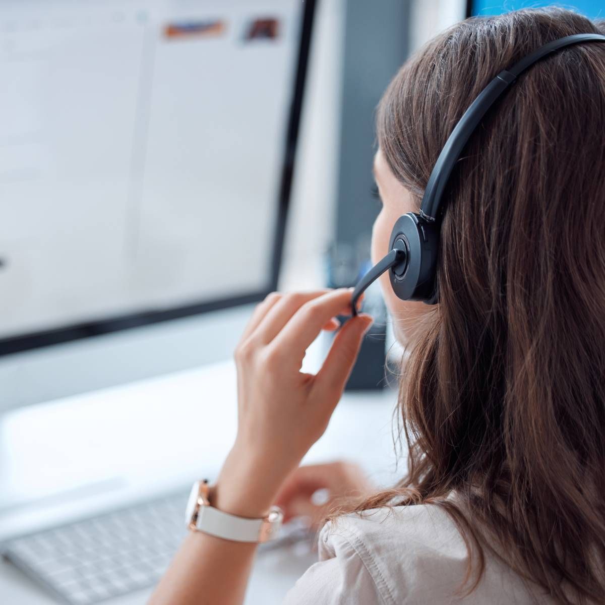 Woman wearing a headset, working at a computer. Her hand touches the microphone.