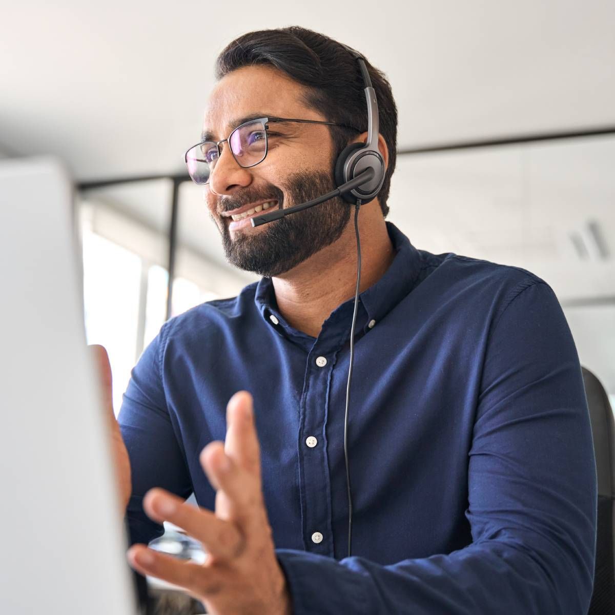 Man wearing headset and glasses, smiling while looking at a computer screen.